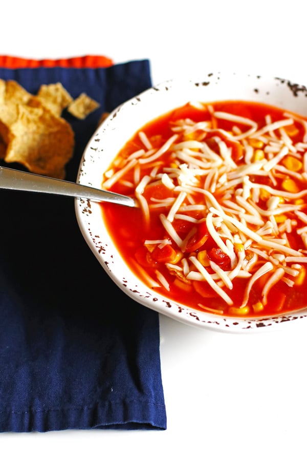 A bowl of soup with shredded mozzarella cheese over the top of it.