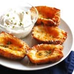 Four potato skins on a white plate with a small bowl of sour cream and chives