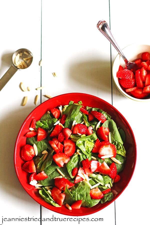 Spinach, slivered almonds and sliced strawberries in a red serving dish