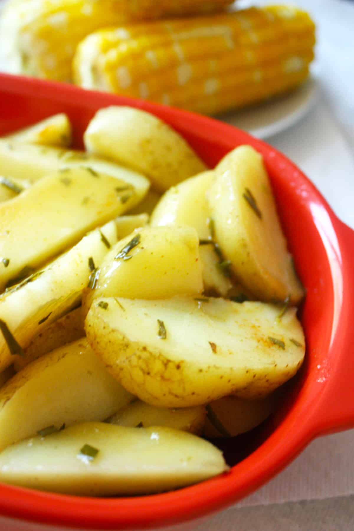 A red bowl of cooked oven roasted rosemary potatoes covered in butter and rosemary.