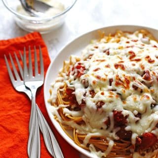 Spaghetti noodles covered in sauce and melted mozzarella cheese on a white plate