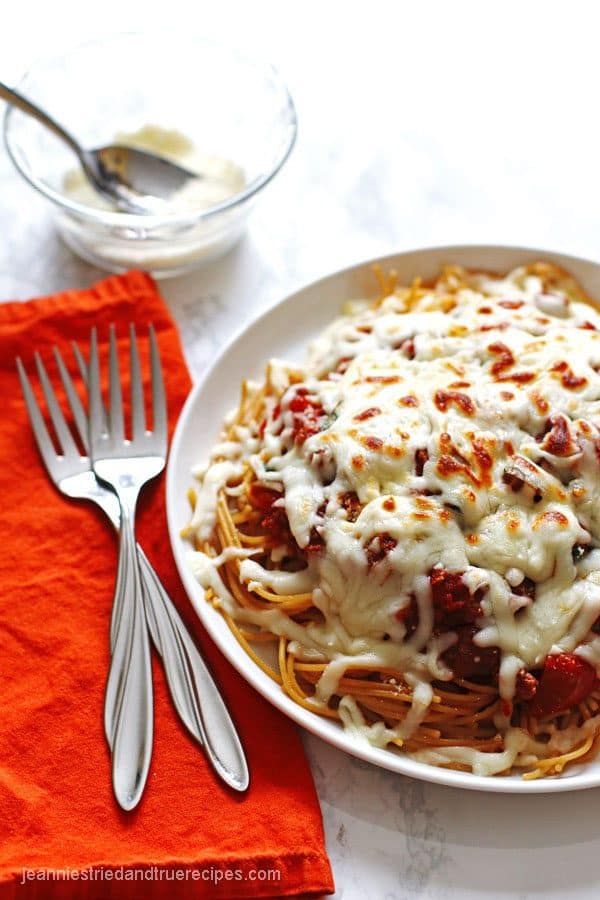 Spaghetti noodles covered in sauce and melted mozzarella cheese on a white plate