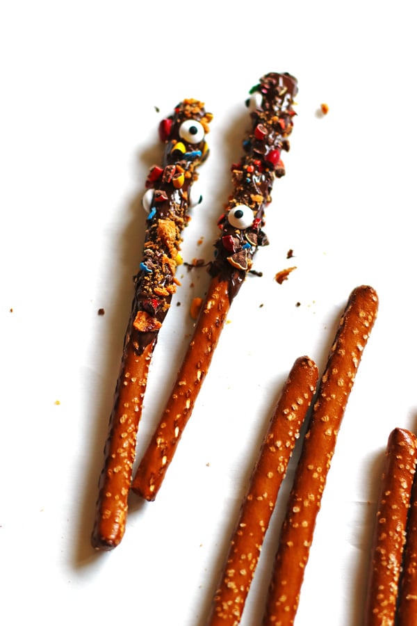 Pretzel Rods on white table. Some are covered with chocolate and crushed up candy. Some are plain pretzels.