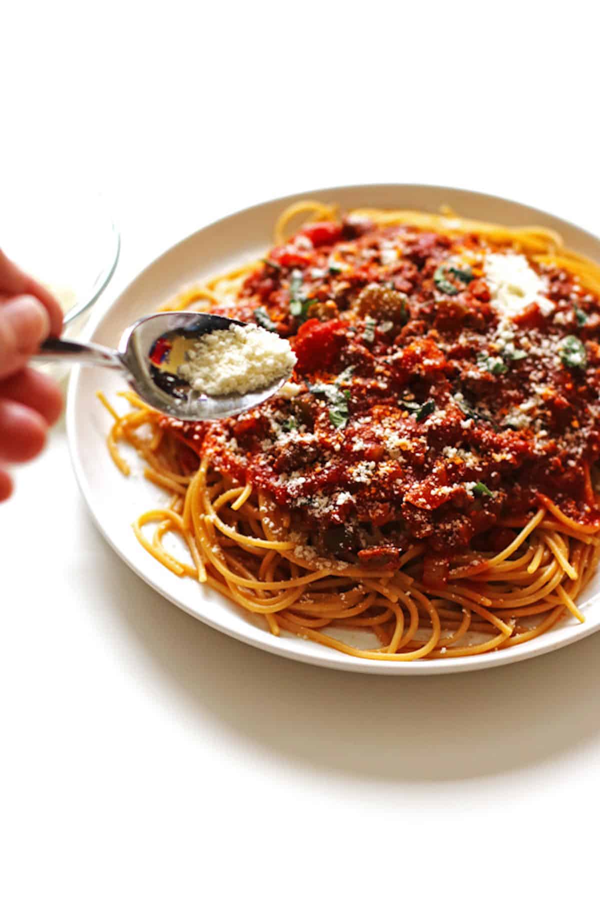 Sprinkling grated Parmesan cheese over a plate full of spaghetti noodles and sauce.