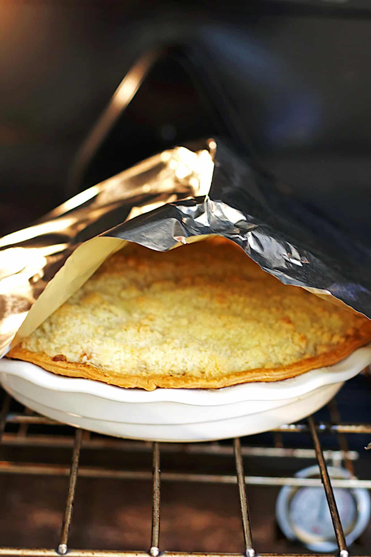 Apple pie in oven with foil tent over the pie
