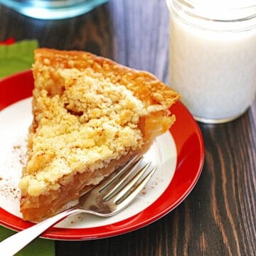 A slice of Dutch Apple Pie on a plate with a glass of milk next to it.