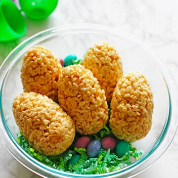 Easter eggs made out of rice krispie treats and filled with M&M's placed in a clear bowl with green easter grass and candy