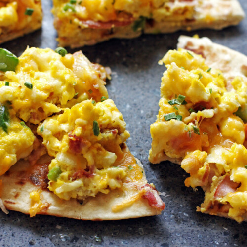 A breakfast pizza with ham, eggs, onions, peppers, & cheese on a tortilla.
