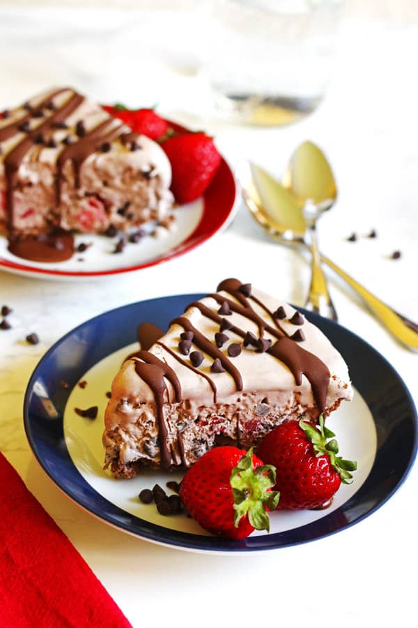 Two slices of ice cream pie. Each slice is on a plate and garnished with strawberries and chocolate chips