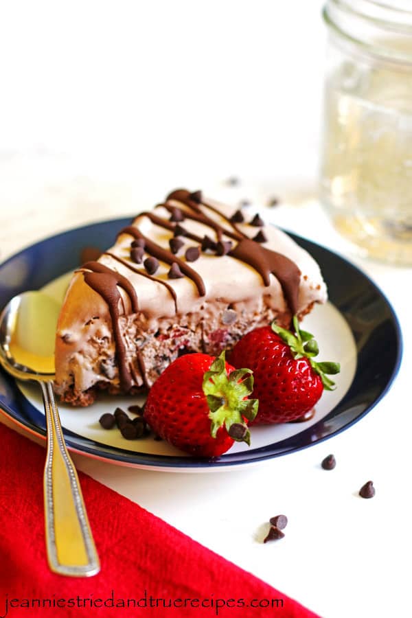 A slice of ice cream pie on a plate with a spoon and two strawberries next to the pie