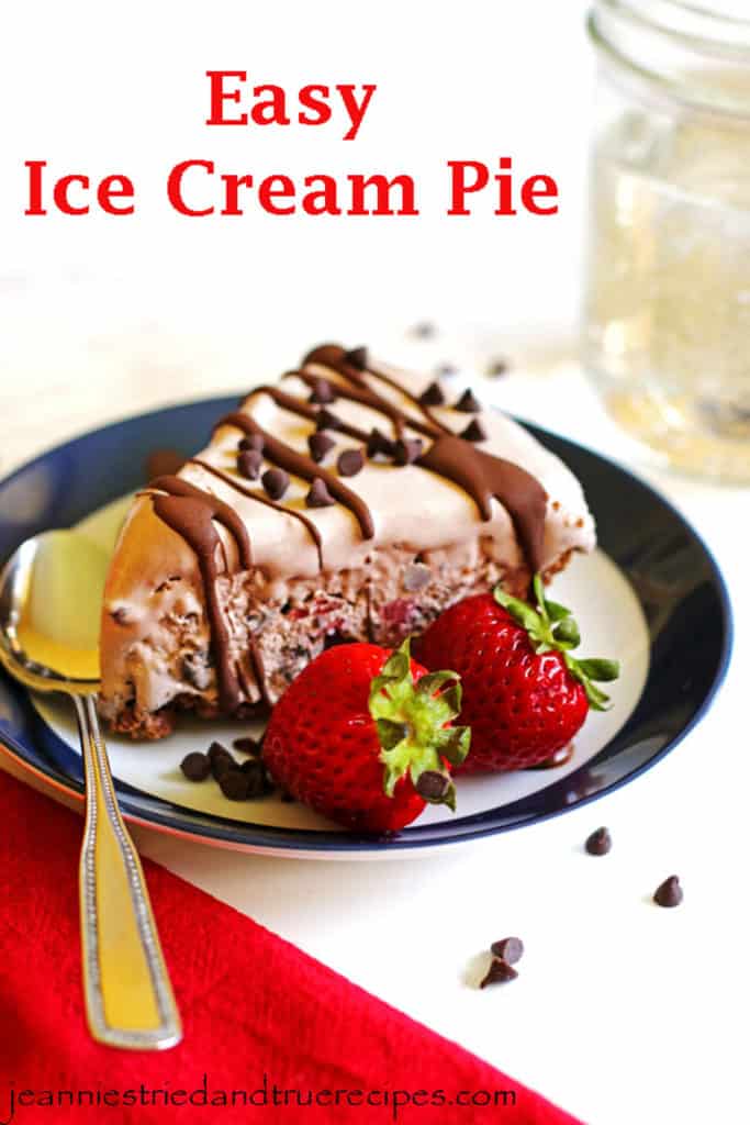 A slice of ice cream pie on a blue rimmed plate. The pie is garnished with chocolate chips, chocolate sauce and strawberries.