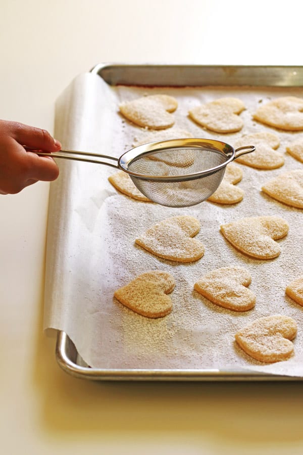 Pie crust cut into hearts on baking sheet getting sprinkled with powdered sugar