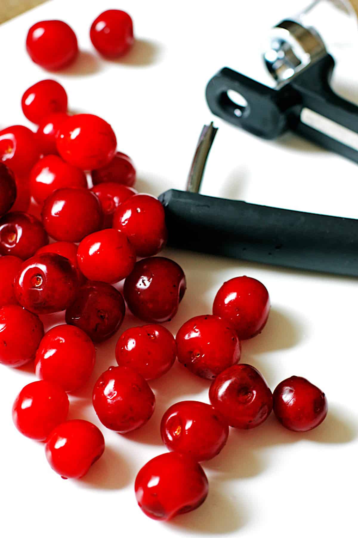 Tart cherries and a cherry pitter on a white counter