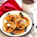 Blueberry Pancakes on a white plate with a mug filled with coffee and extra blueberries near the plate