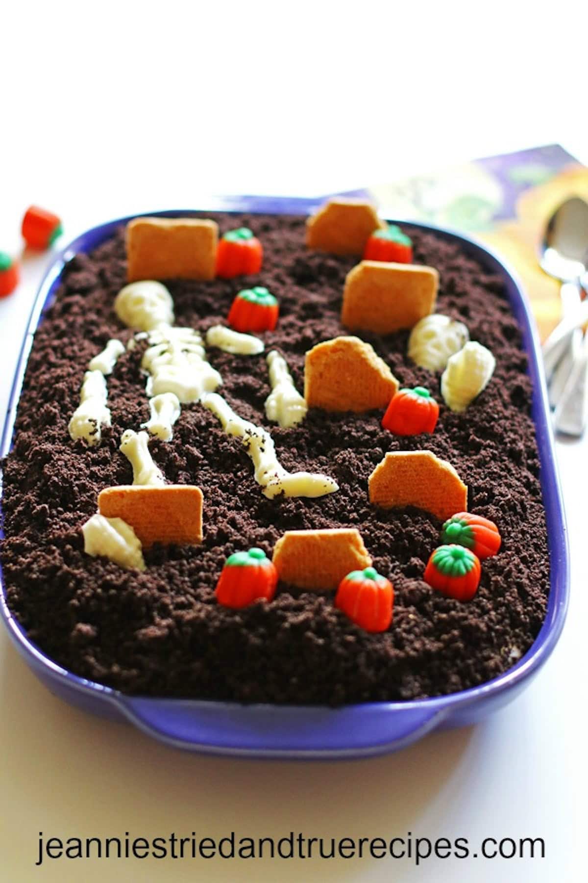 Dirt cake in a baking dish.. It is decorated as a graveyard with crushed up oreos as dirt. It also has candy pumpkins and cookies to look like gravestones.