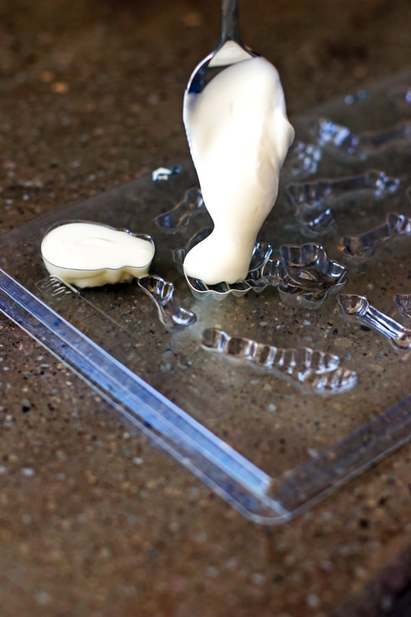 Pouring melted white chocolate into skeleton candy mold with a spoon