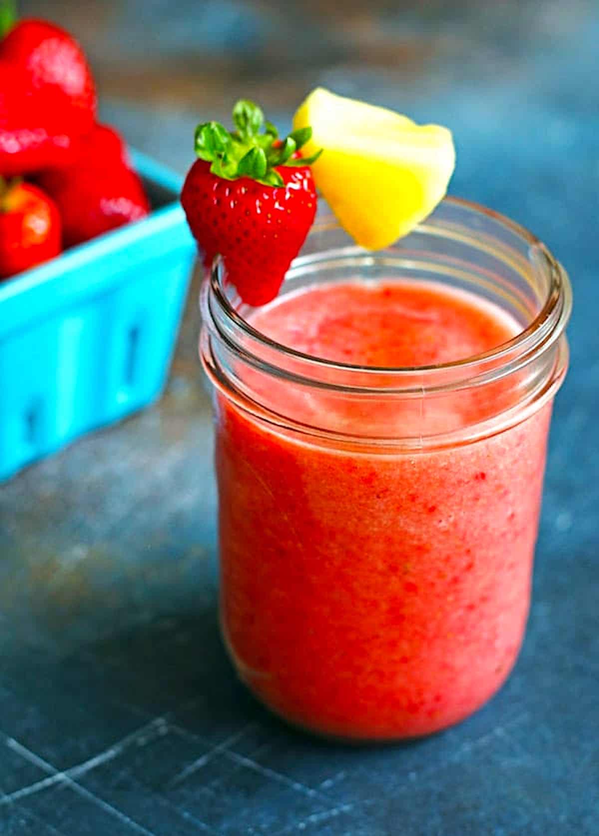 smoothie in a glass with sliced strawberry and pineapple along the rim of the glass