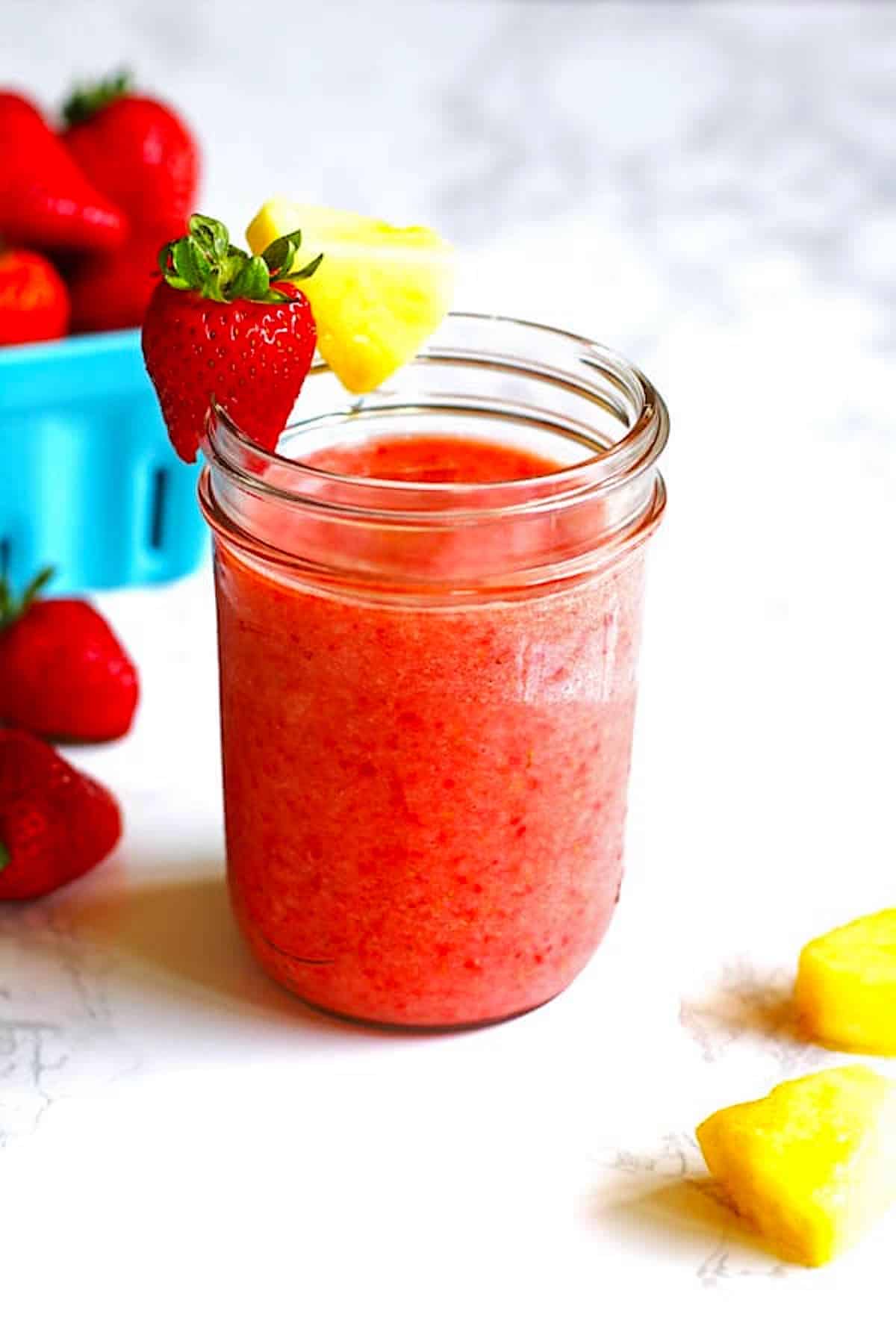 Smoothie in a glass with strawberry and pineapple along the rim of the glass