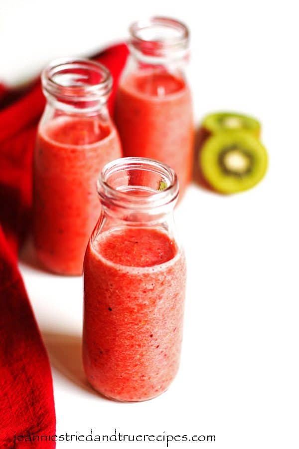 Kiwi Smoothie in three clear glasses with a kiwi sliced in half next to them with a red napkin