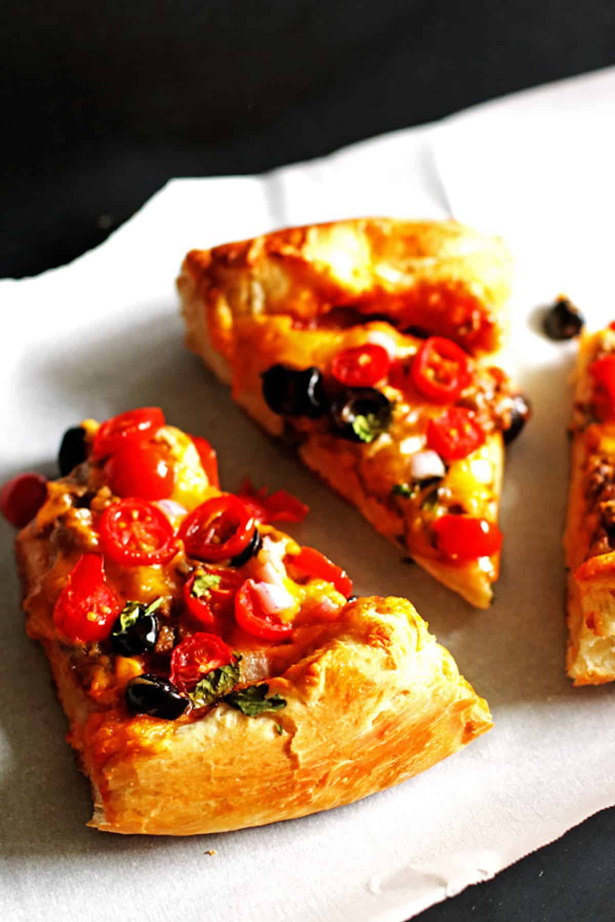 Three slices of taco pizza topped with tomatoes, cilantro, and black olives.