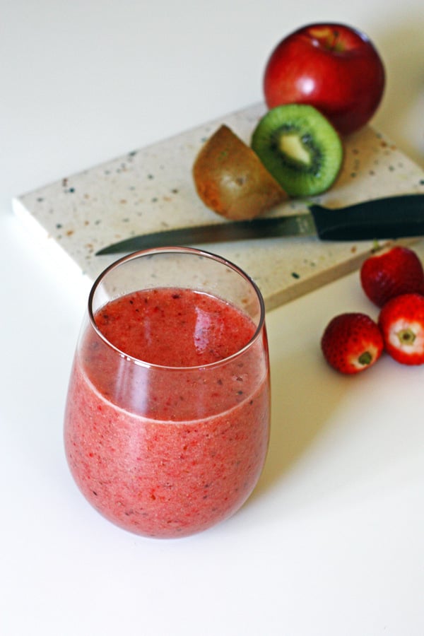 Smoothie with sliced fruit on cutting board with a knife