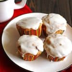 Four carrot cake muffins on a white plate with a red napkin and mug with milk next to the plate