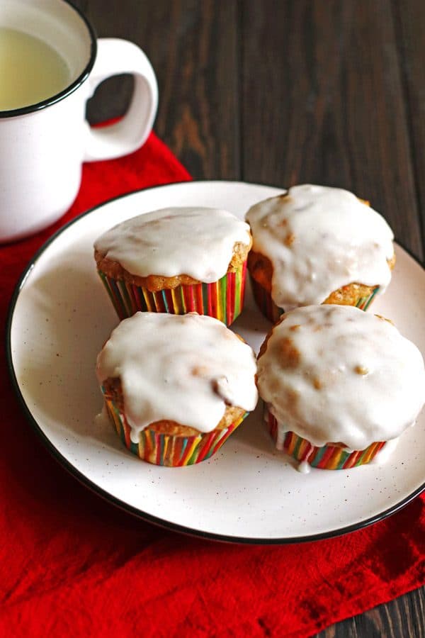 Four carrot cake muffins on a white plate with a red napkin and mug with milk next to the plate
