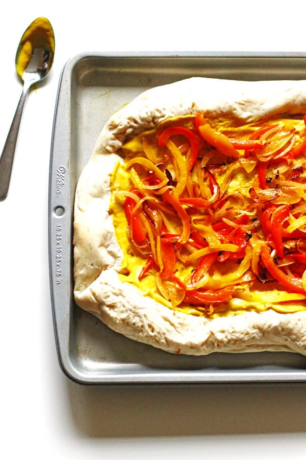 Sliced peppers and onion over mustard on pizza dough placed a baking pan