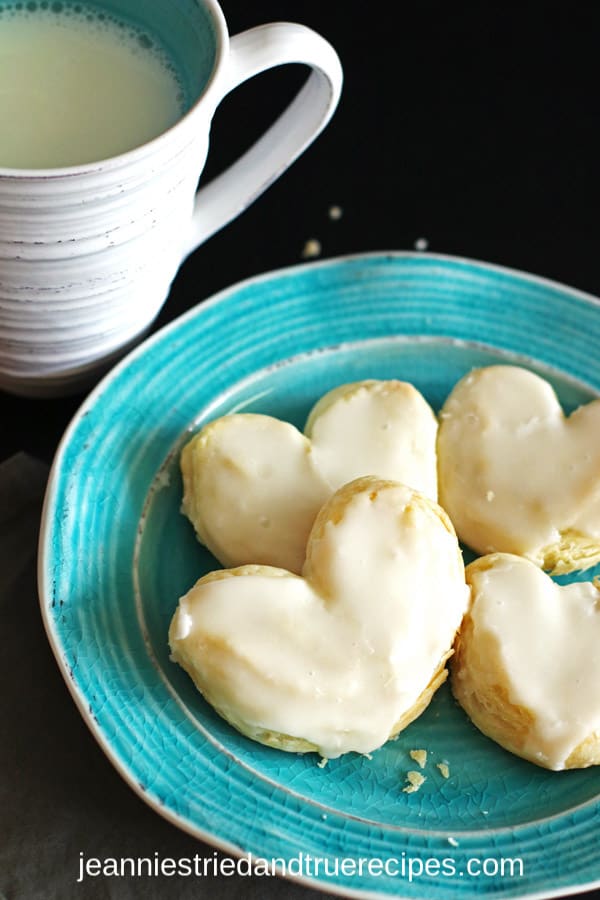 Frosted puff pastry hearts on a turquoise plate with a glass of milk