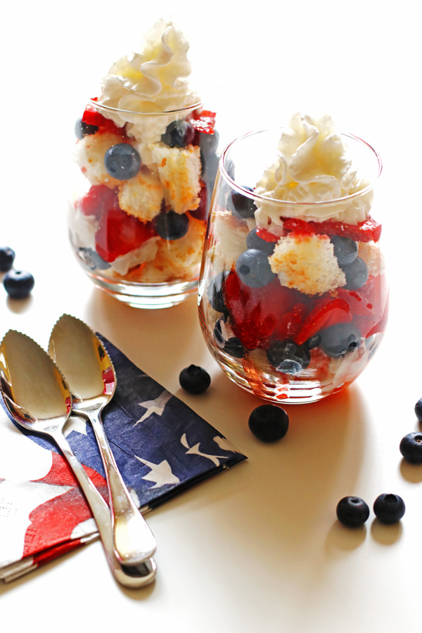 Blueberries, strawberries, whipped cream and toasted angel food cake layered in clear glasses with spoons and flag napkins next to them.