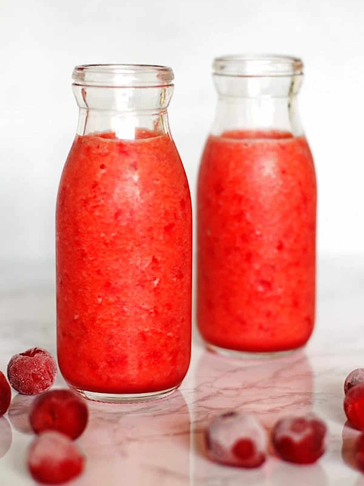 Cherry Smoothie in two clear glasses with frozen cherries on the counter next to the glasses