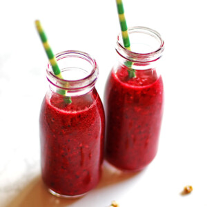 Two cherry pineapple smoothies in small bottles with green and yellow straws.