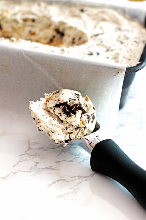 Homemade Ice Cream in a loaf pan with an ice cream scoop next to it. The ice cream scoop has cookies and cream ice cream in it.