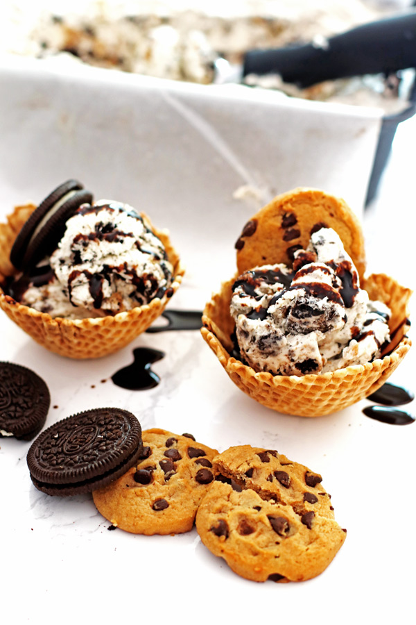 Cookies and cream ice cream in waffle bowls with chocolate syrup drizzled over the ice cream.