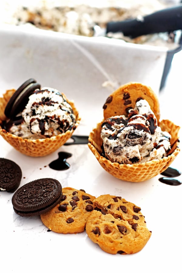 Cookies and cream ice cream in waffle bowls with chocolate syrup drizzled over the ice cream.