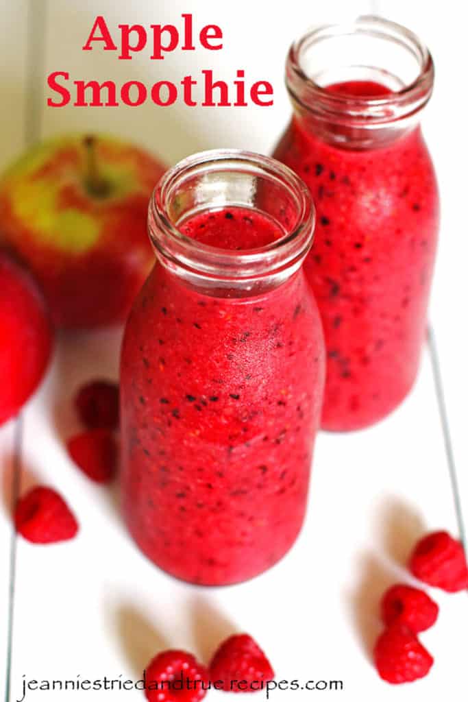 Apple Smoothie in clear glasses on a white table with apples and raspberries next to them.