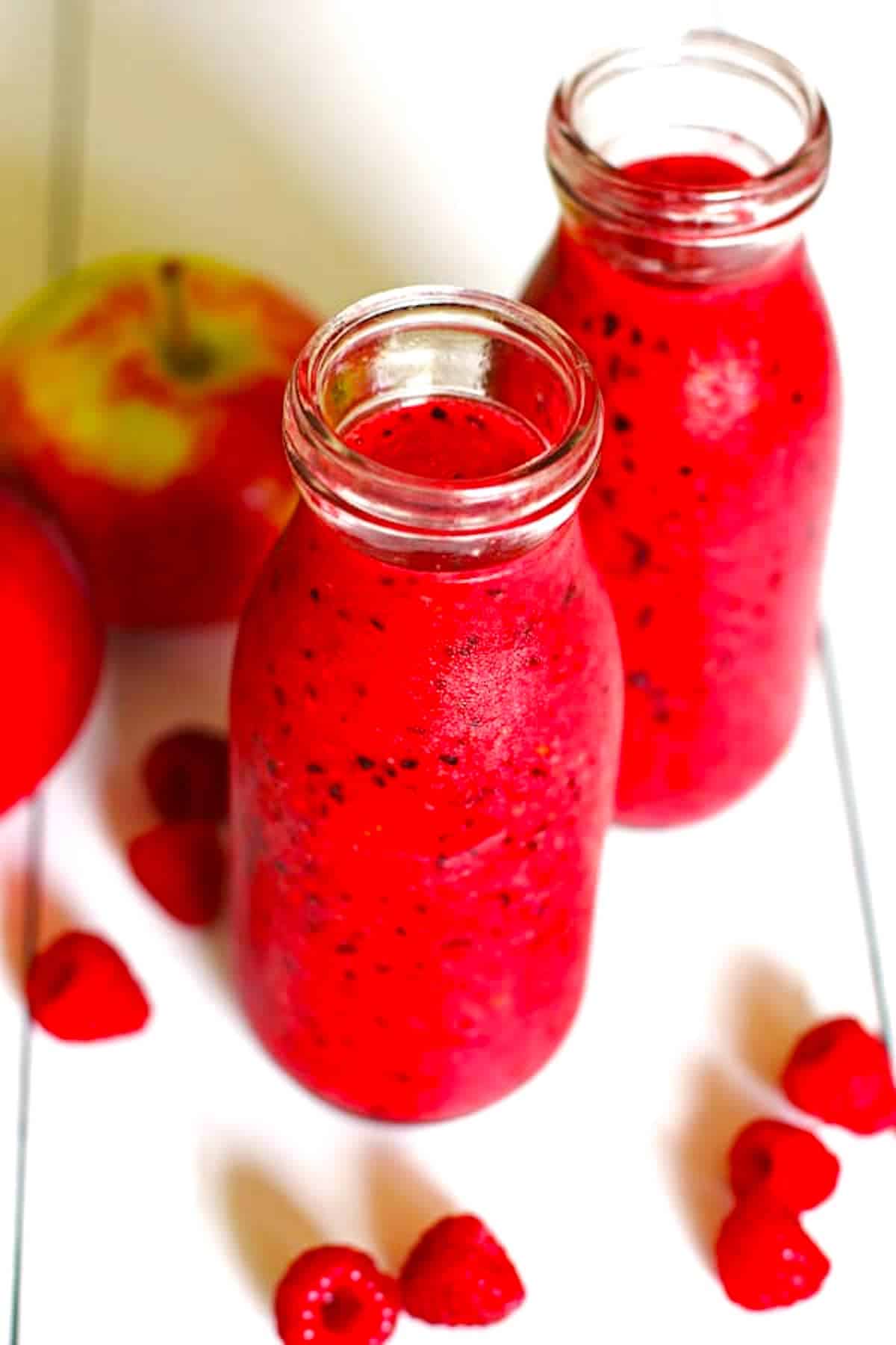 A red smoothie made of apples and berries that is sitting on a white table.