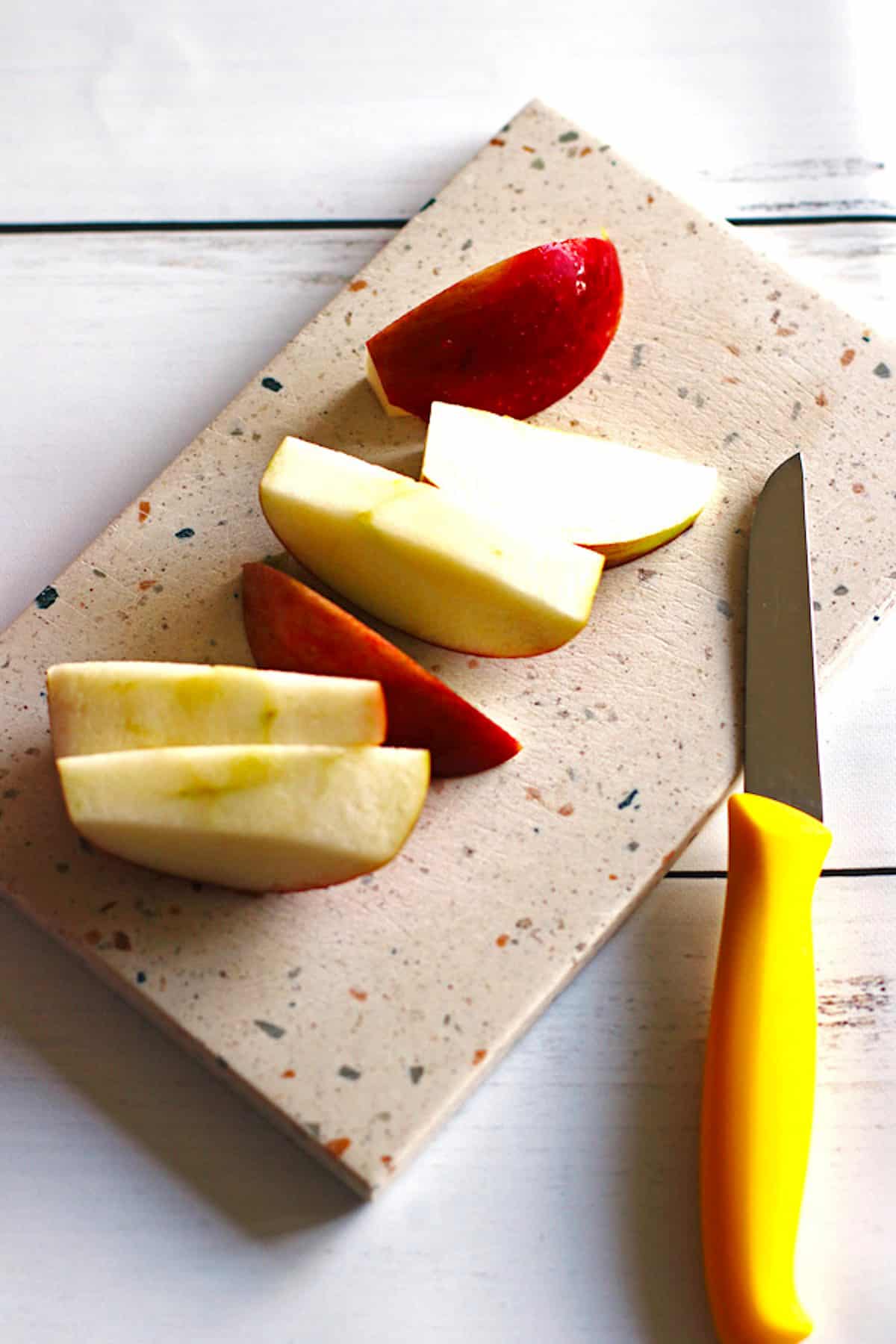 An apple sliced into medium pieces on a cutting board with a knife