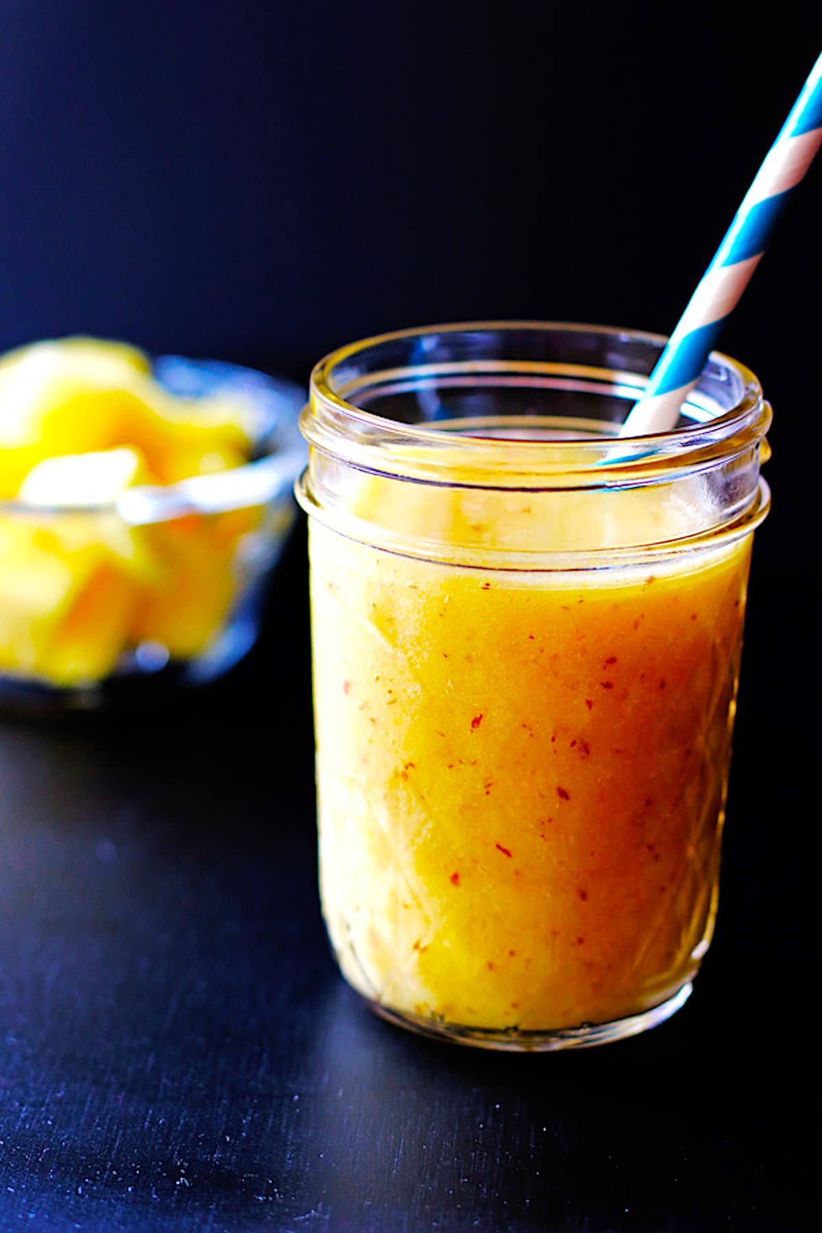 A tropical smoothie in a mason jar with a blue straw.