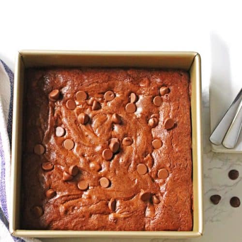 Homemade brownies in an 8 x 8 pan with plates and spoons next to it