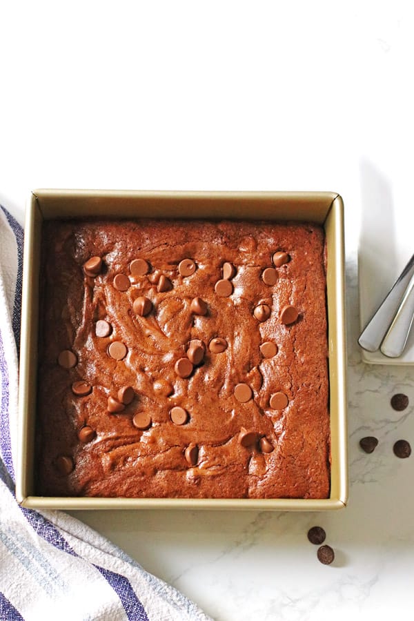 Homemade brownies in an 8 x 8 pan with plates and spoons next to it