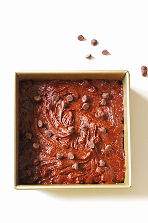 Brownie batter in square pan with chocolate chips placed on top