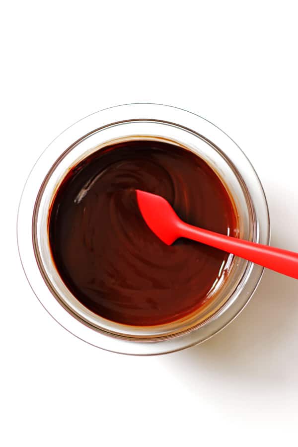 Melted butter and baker's chocolate in a clear bowl with a red spoon