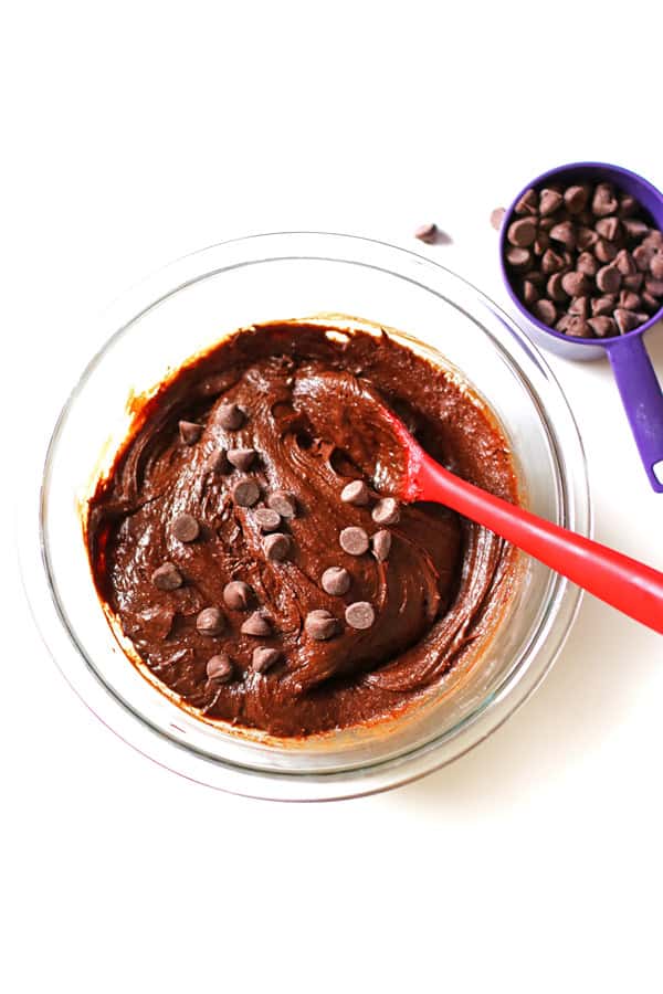 Homemade brownie ingredients in a clear mixing bowl with chocolate chips being added to the batter