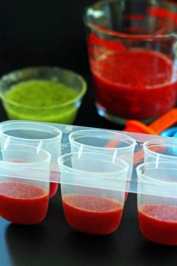 Strawberry and Kiwi puree in pyrex containers with popsicle molds partly filled up