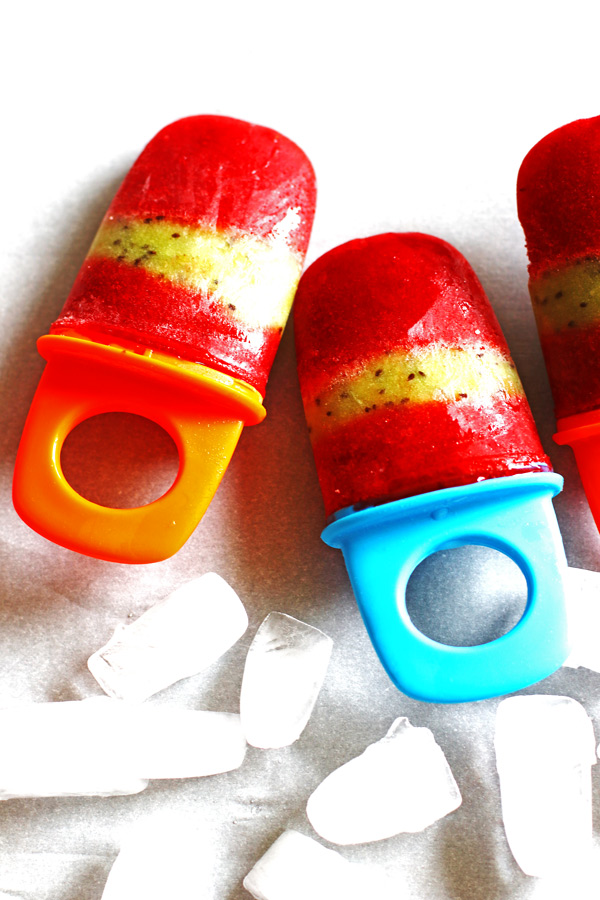 Fruit Popsicles on a white counter with ice cubes laying next to them