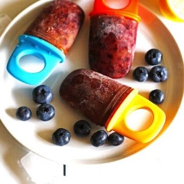 Homemade healthy popsicles on a white plate with blueberries.