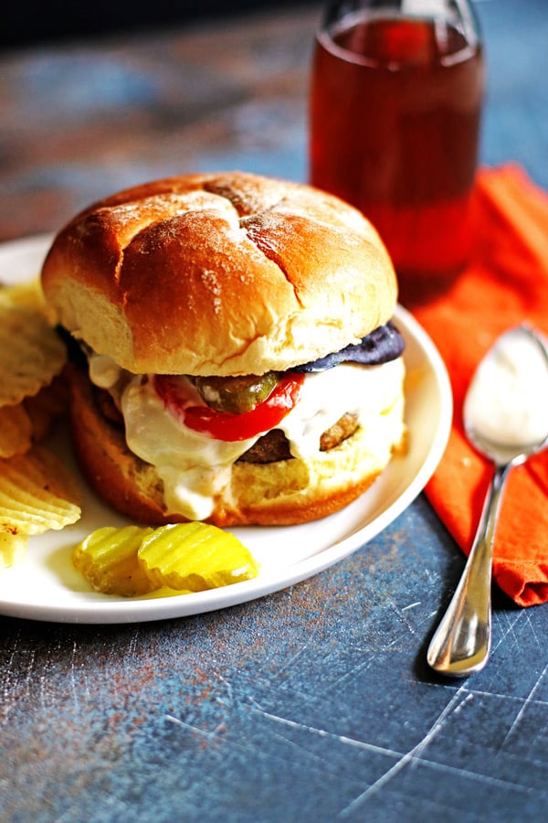 Blue Cheese Burger on a roll with tomaot and pickles and extra blue cheese dressing on a white plate. 