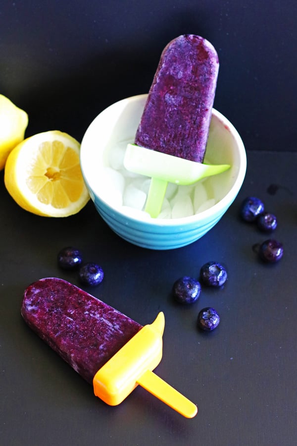 Homemade popsicles in a bowl filled with ice and also laying on a black table.