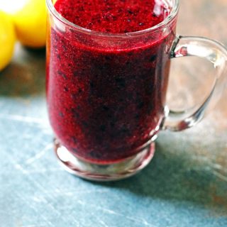 Blueberry smoothie in a mug with two lemons behind it